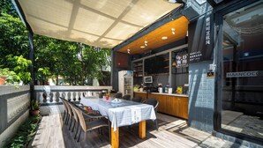 An outdoor dining area with a table and chairs, a wooden deck, and a building with a sign that reads "MAANCOCO". - Maan Coco Travelling Boutique Inn (Shenzhen)
