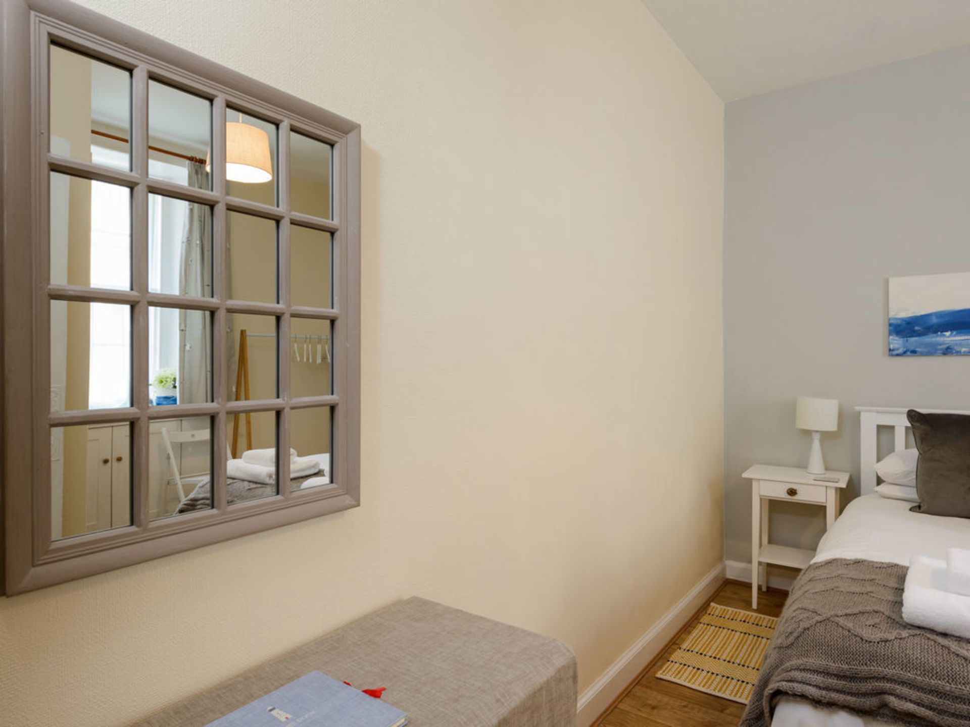 A hotel room with a large window, a bed with a pillow, a bedside table with a lamp, and a small rug.
