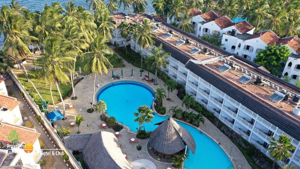 Un resort con una gran piscina, palmeras y un edificio blanco con techo de tejas.