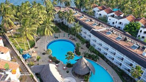 A resort with a large swimming pool, palm trees, and a white building with a tiled roof.