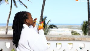 Una persona disfrutando de una bebida con vistas a la playa y palmeras.