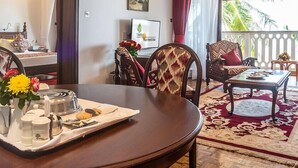 Un comedor con una mesa redonda, sillas y una bandeja con condimentos. Se ve una ventana con cortinas y vistas a palmeras.