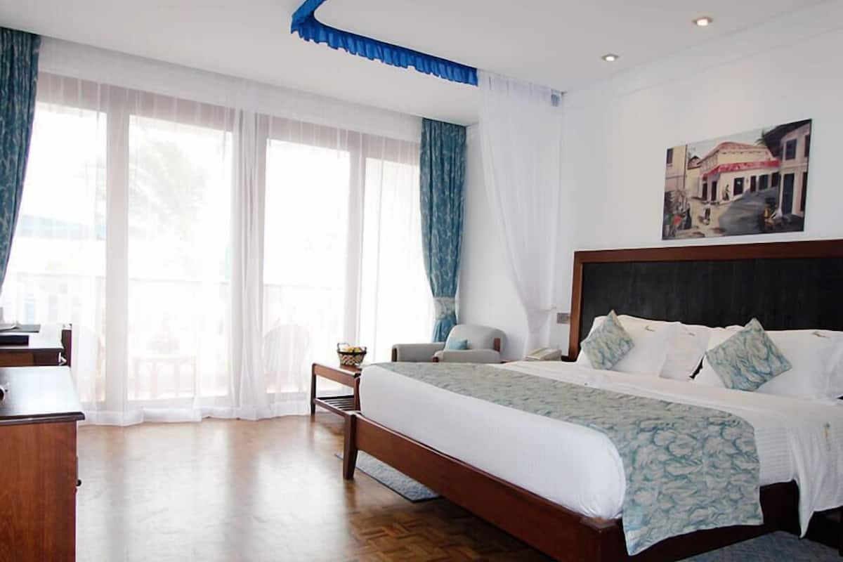 Habitación de hotel con una cama grande, un escritorio y una silla. Hay una ventana con cortinas y un cuadro en la pared.