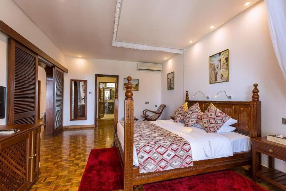 Un dormitorio con cama con dosel, suelo de madera y alfombra roja.