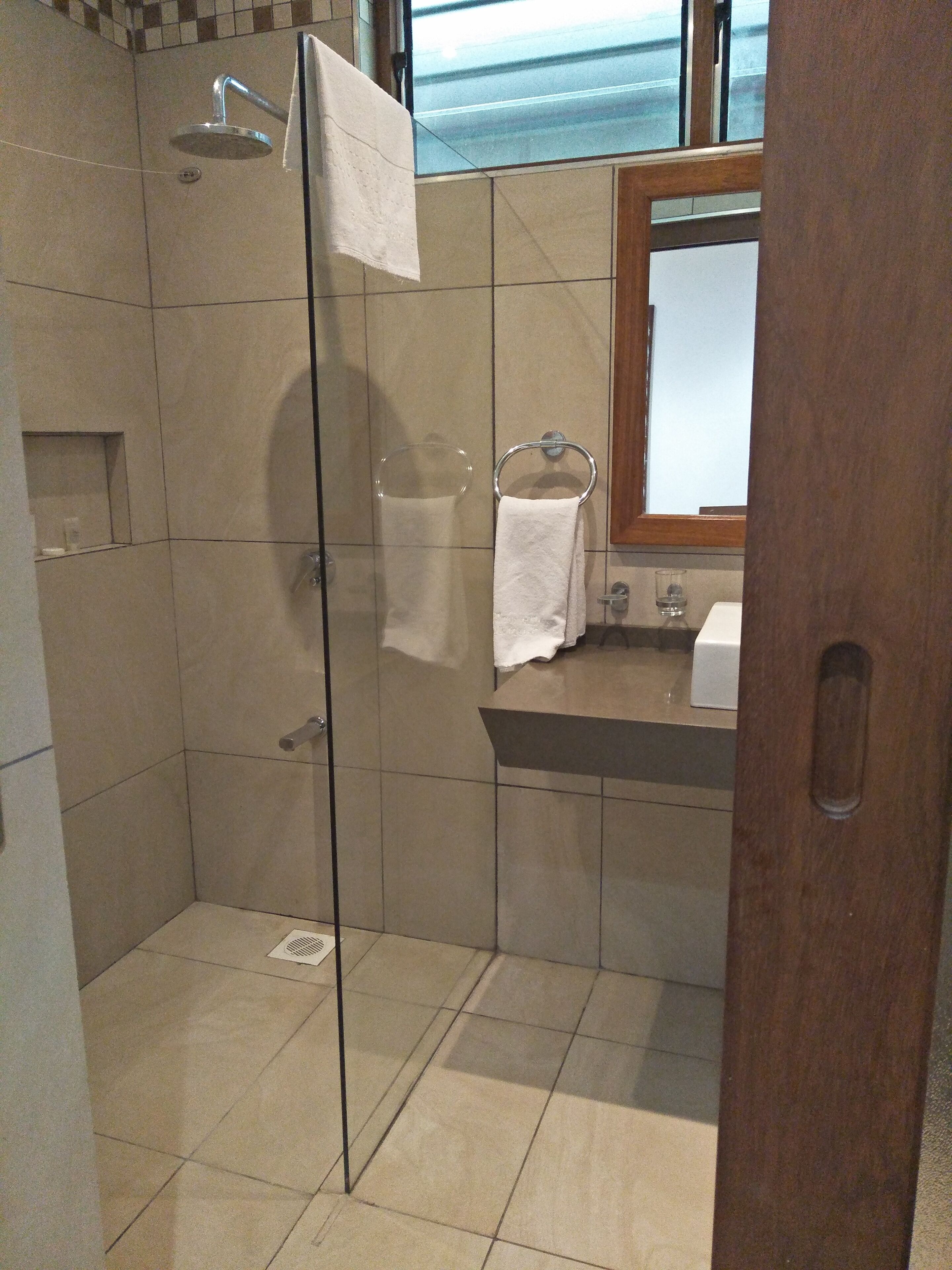 Uma casa de banho moderna com cabine de duche em vidro, espelho com moldura de madeira e chão em mosaico.