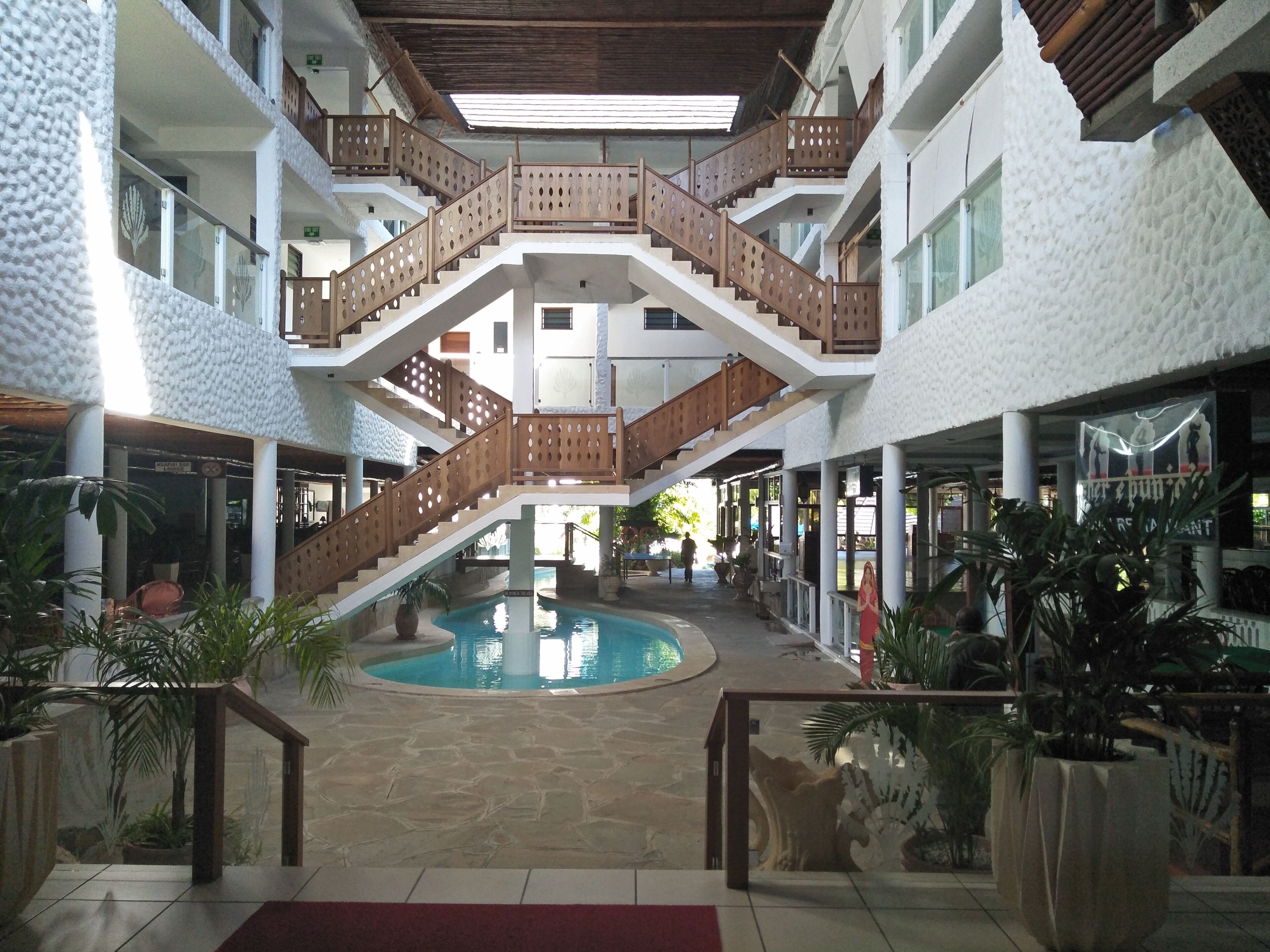 A multi-level indoor area with a central pool, wooden railings, and potted plants.