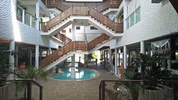 A multi-level indoor area with a central pool, wooden railings, and potted plants.