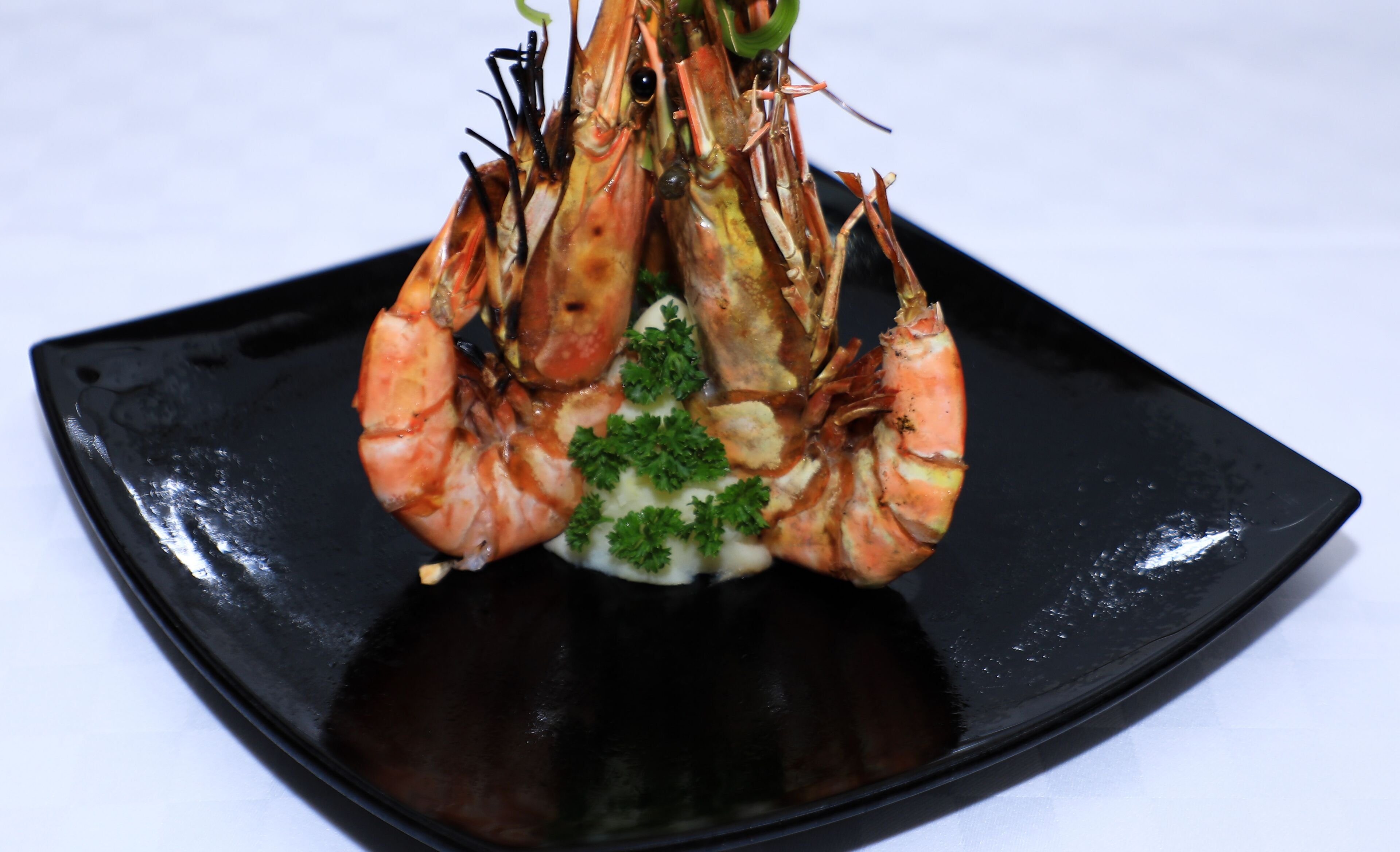 A black square plate with three cooked shrimp garnished with parsley.