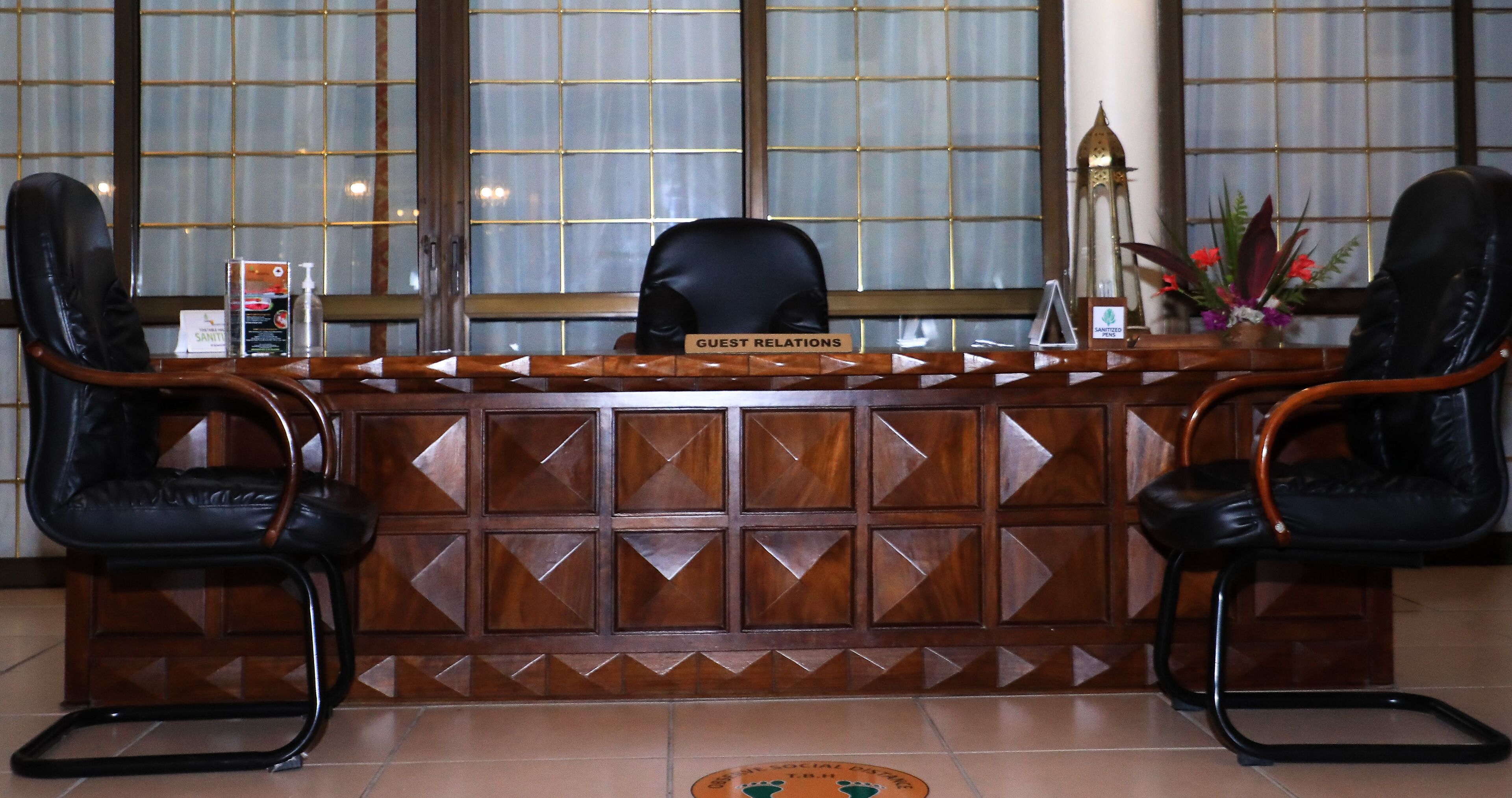 Um balcão de recepção com uma placa indicando 'Guest Relations' e duas cadeiras de couro preto de cada lado.