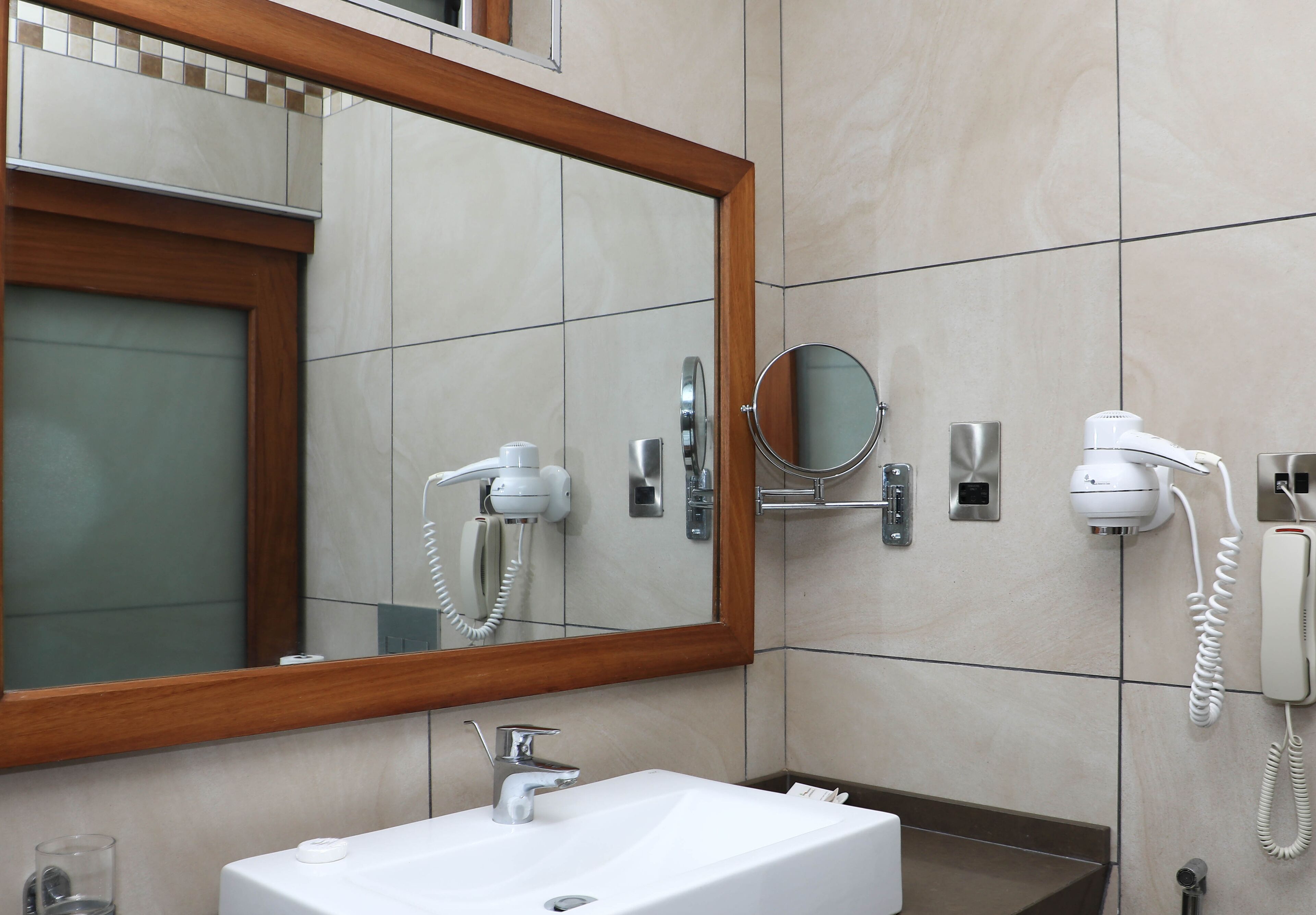A modern bathroom with a large mirror, a white sink, and two hair dryers mounted on the wall.