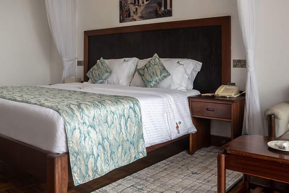Habitación de hotel con cama, mesita de noche, escritorio y un cuadro en la pared.
