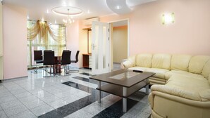 A modern living room with a beige sofa, a glass coffee table, and a dining area with chairs and a chandelier. - Prestige Apart Hotel (Chisinau)