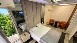 A modern hotel room with a large bed, a small desk, a chair, and a view of greenery outside. - Prestige Apart Hotel (Chisinau)