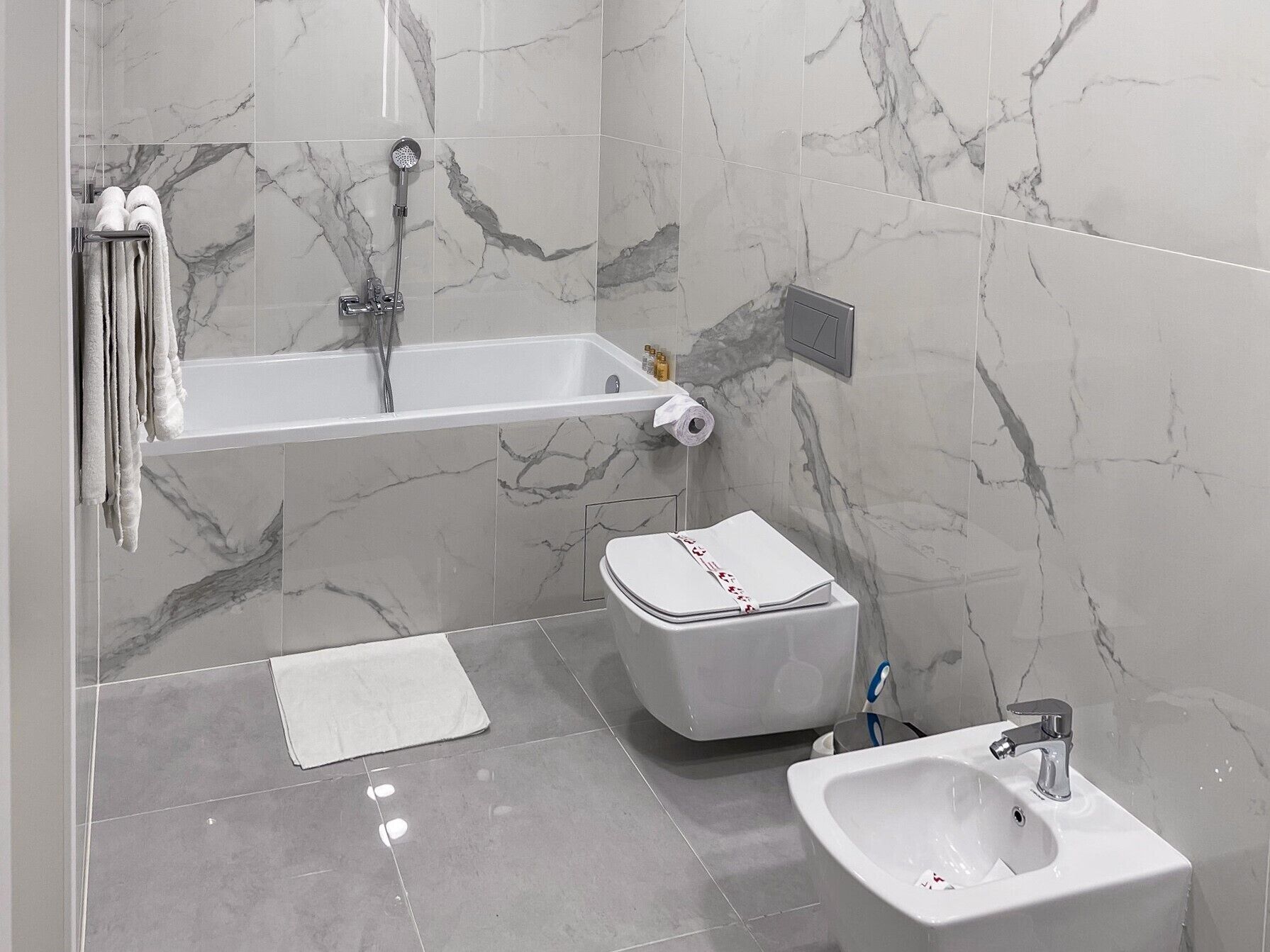A modern bathroom with a bathtub, toilet, bidet, and a small sink.