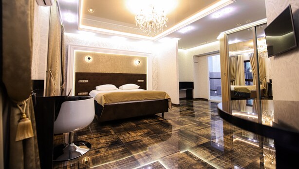 A modern hotel room with a large bed, a sitting area, a TV, and a mirror. - Prestige Apart Hotel (Chisinau)
