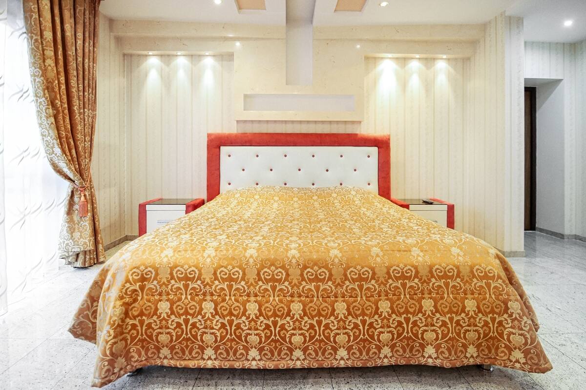 A hotel room with a large bed, a red headboard, and a white wall with a built-in shelf.
