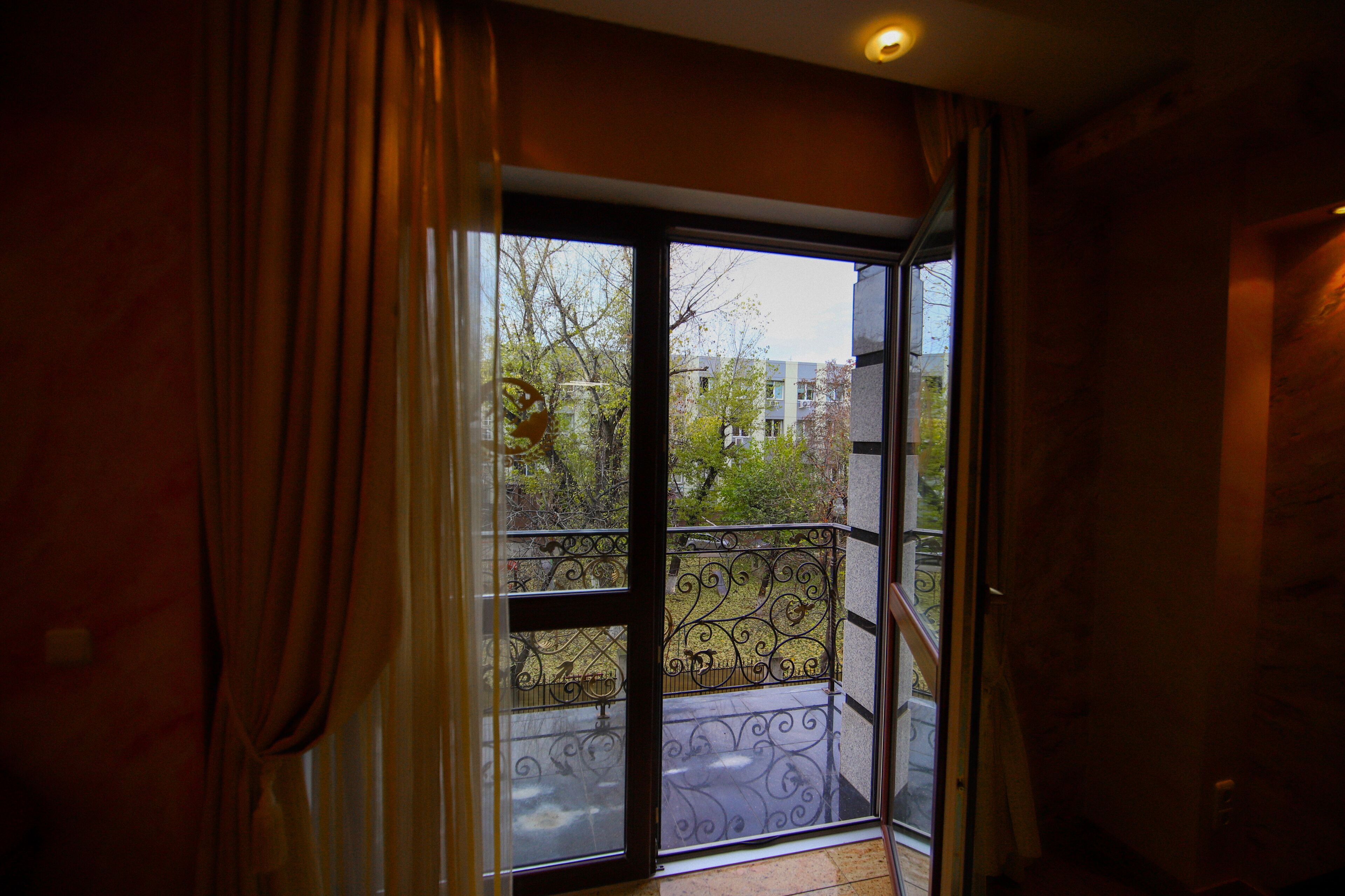 Een kamer met een schuifglazen deur die uitkomt op een balkon met decoratieve ijzeren hekken.