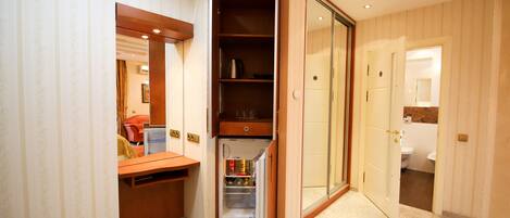 A compact hotel room with a built-in wardrobe, a small kitchenette, and a bathroom visible through an open door.