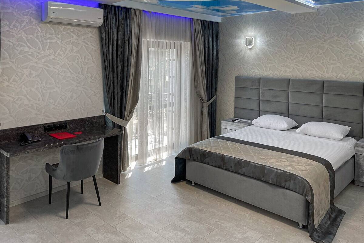 A modern hotel room with a bed, desk, chair, and curtains.