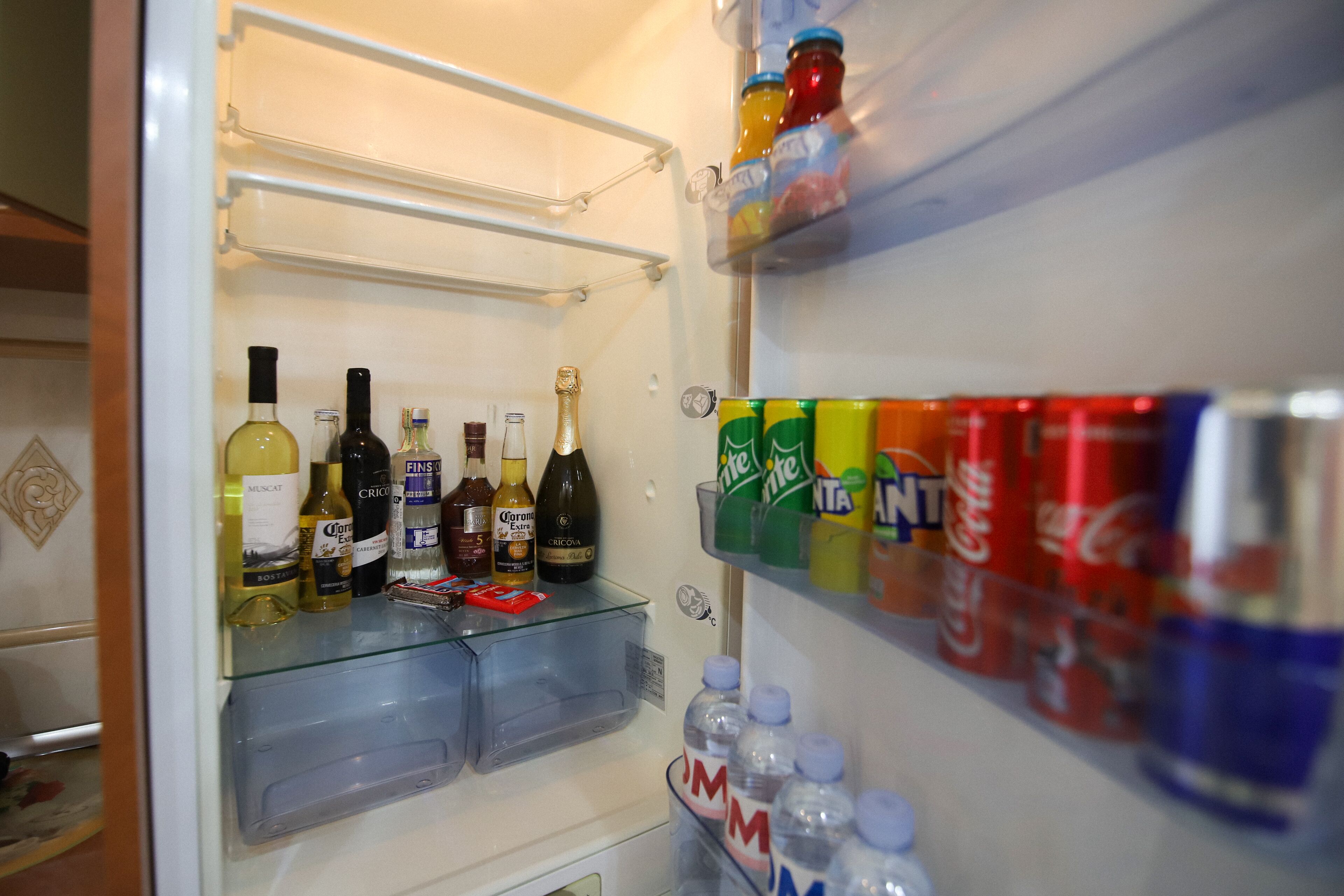 Un refrigerador con estantes que contienen diversas bebidas, incluidas botellas y latas.
