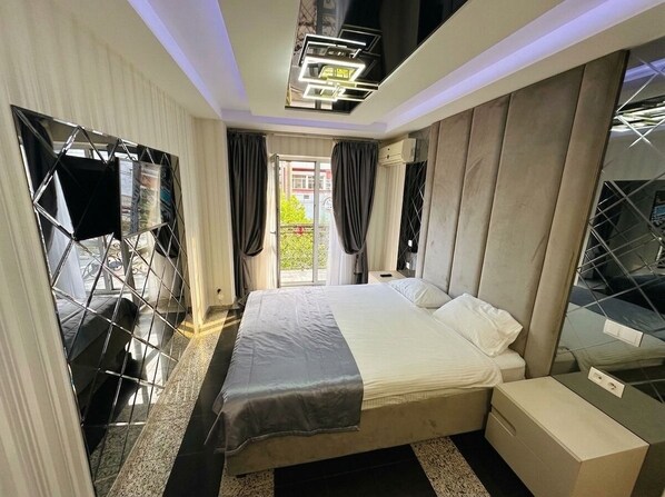 A modern bedroom with a large bed, a bedside table, a mirror, and a view of the outdoors. - Prestige Apart Hotel (Chisinau)
