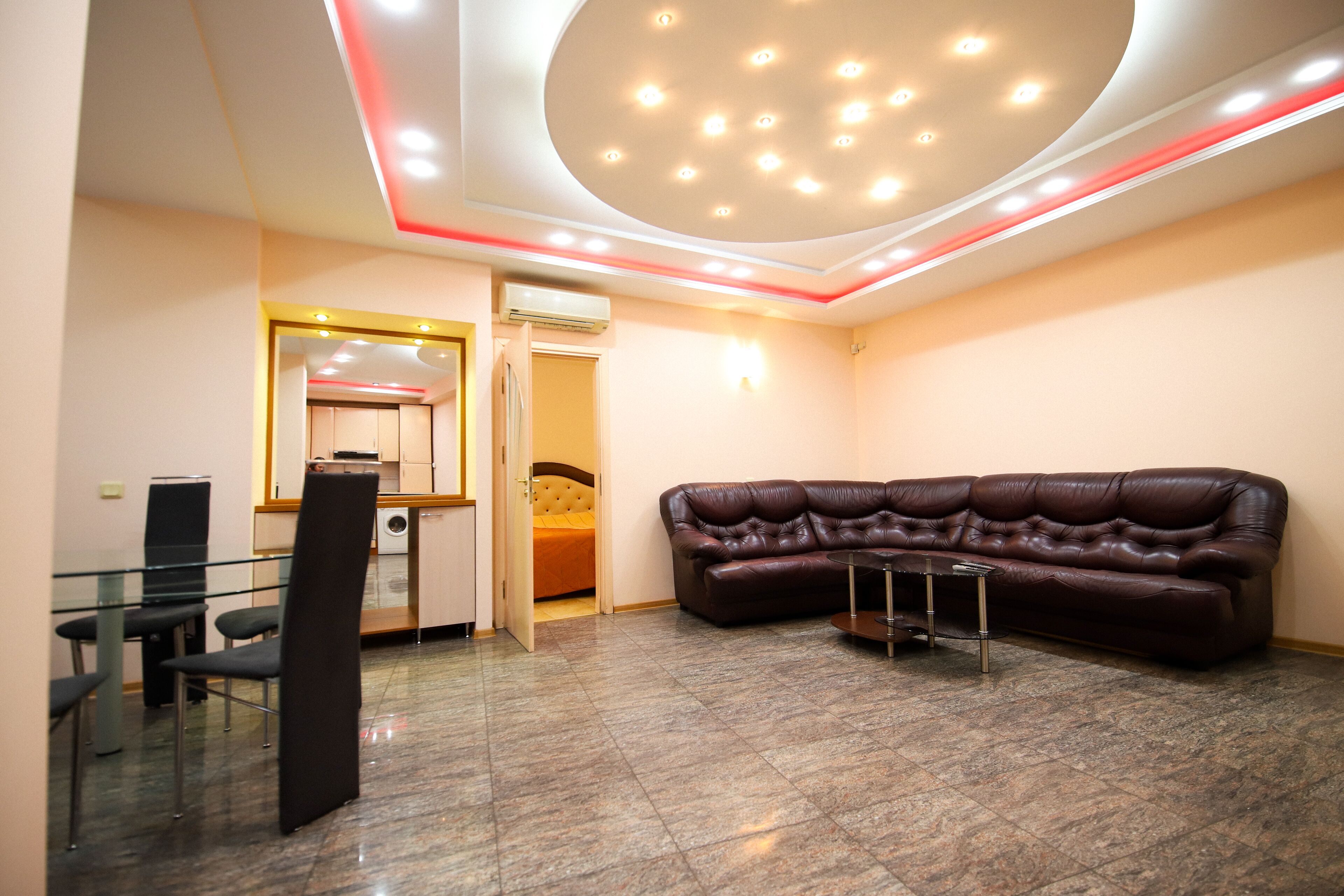Ein modernes Wohnzimmer mit einem braunen Ledersofa, einem Glastisch und einem Essbereich mit Stühlen und einem Tisch.