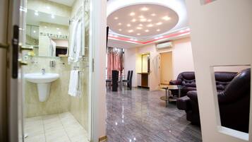 A modern hotel lobby with a glass-enclosed shower, a seating area with leather chairs, and a reception desk.