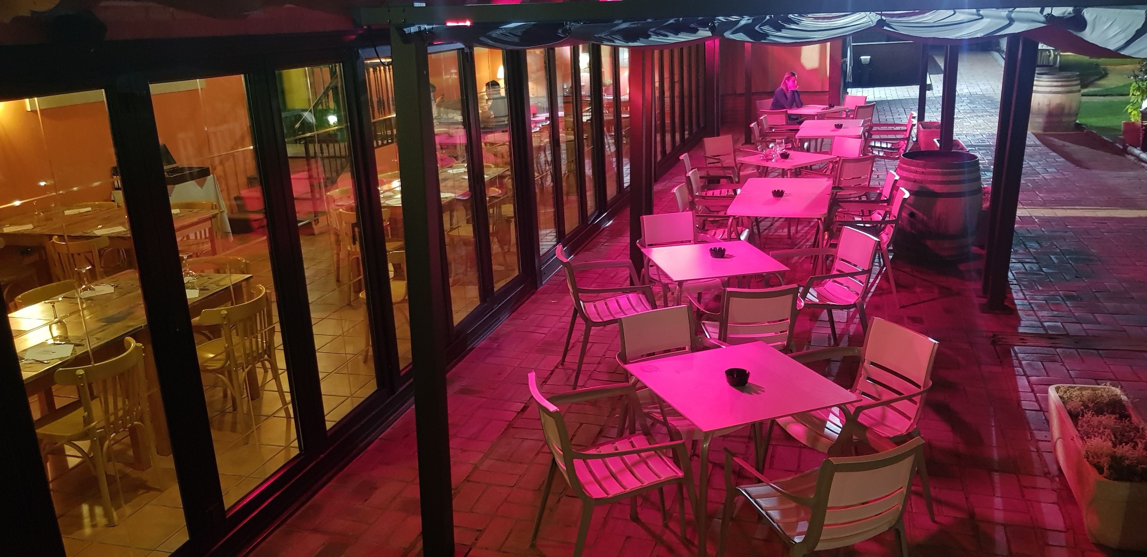 An outdoor dining area with tables and chairs, a view of the street, and a building with large windows.