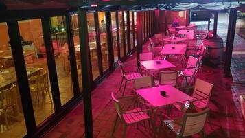 An outdoor dining area with tables and chairs, a view of the street, and a building with large windows.