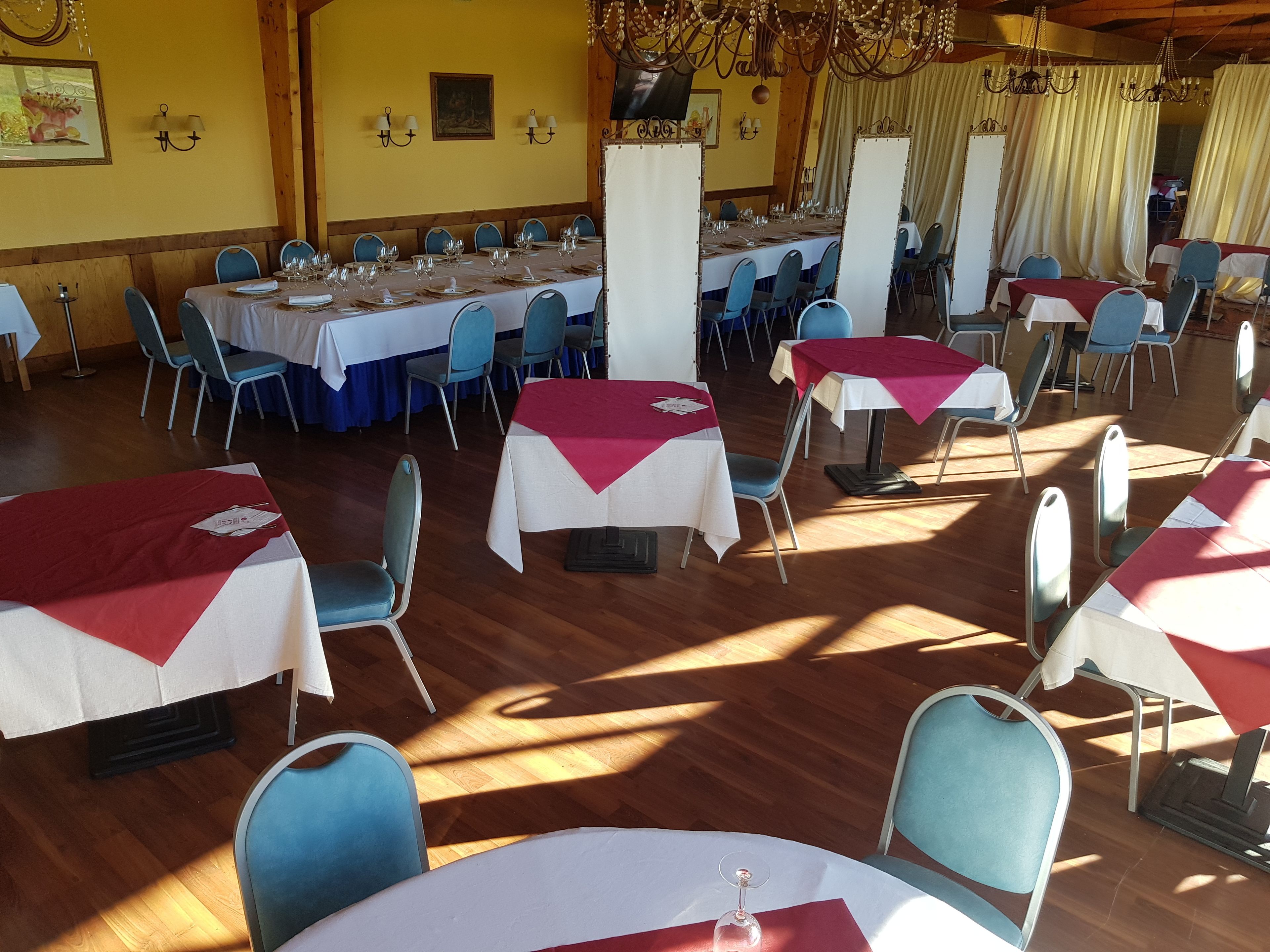A dining hall with multiple tables, blue chairs, and chandeliers.