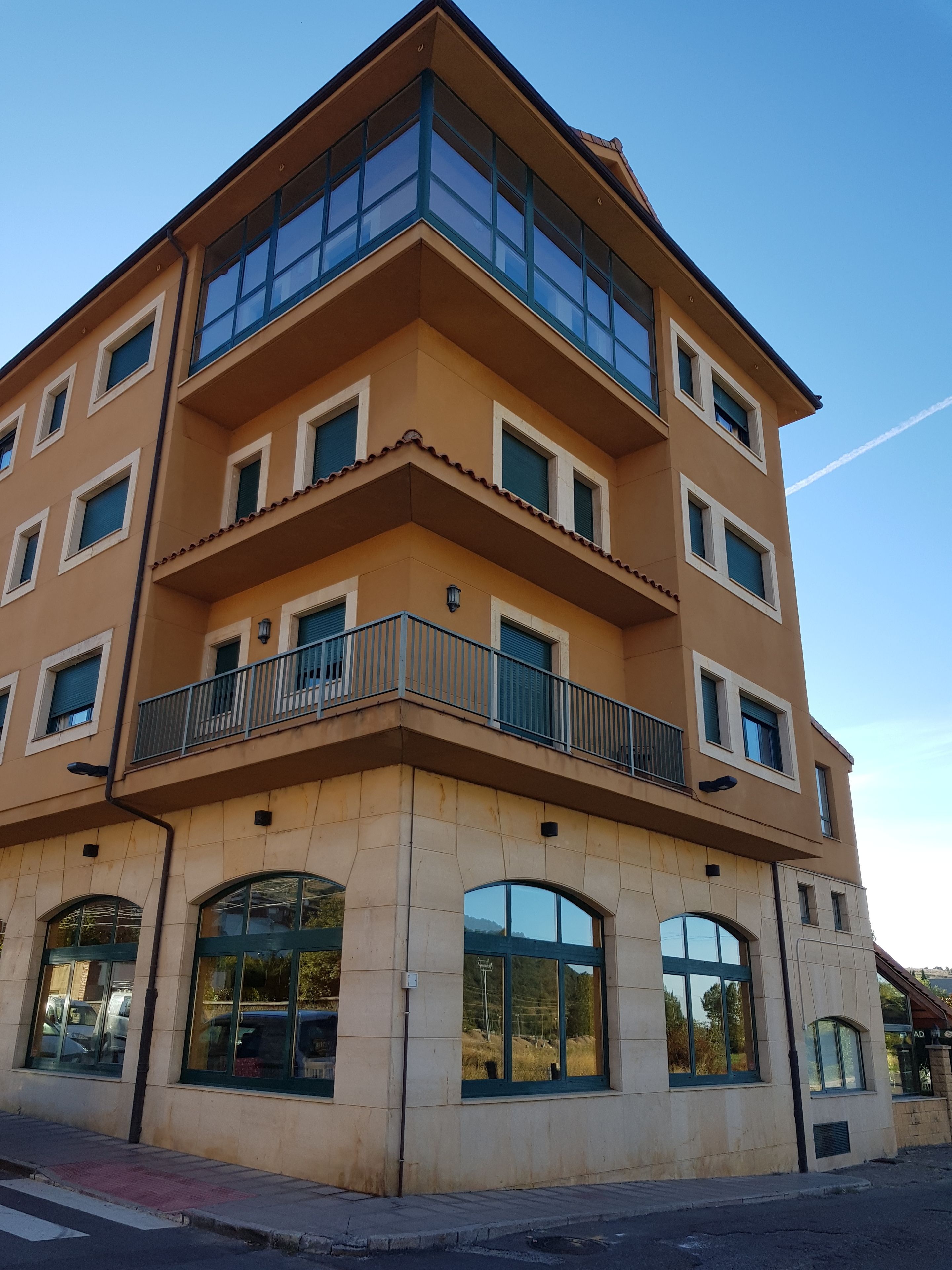 Un edificio de varios pisos con fachada color beige, ventanas grandes y un balcón con barandilla de metal.