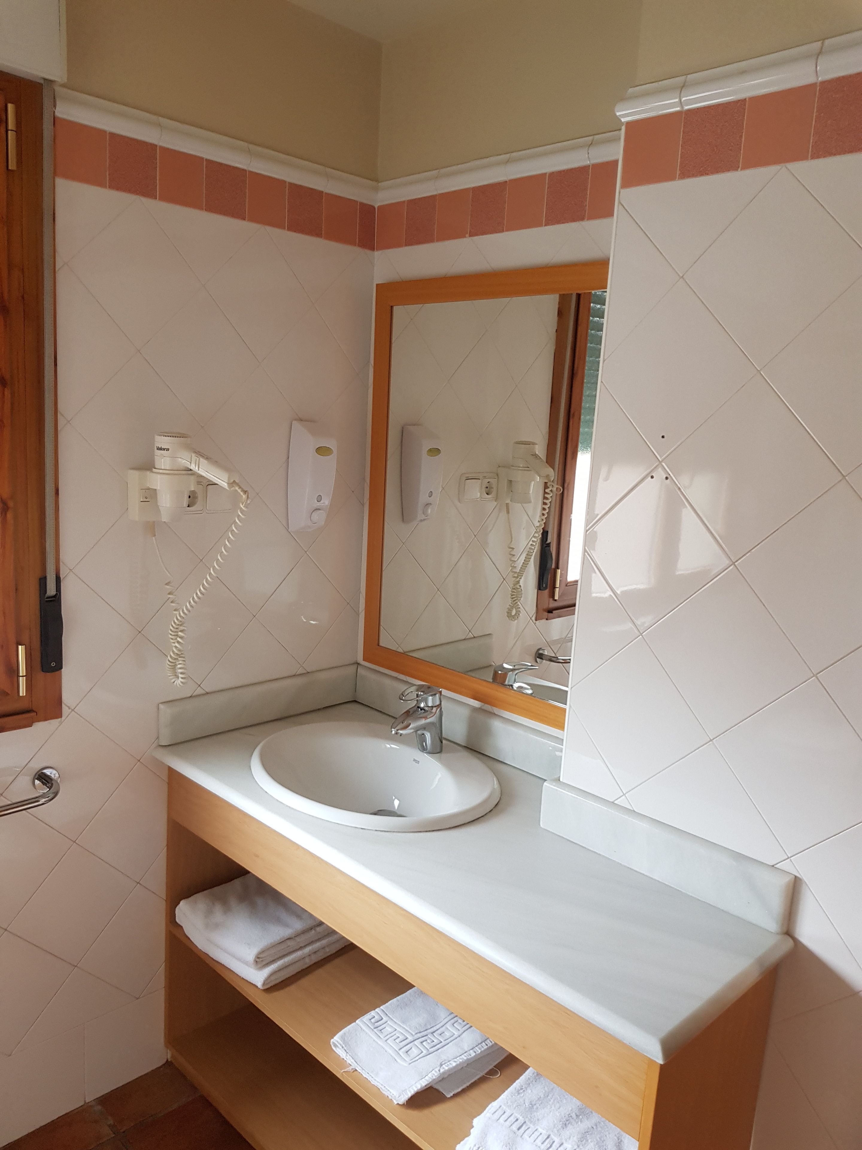 Un baño con lavamanos blanco, tocador de madera y espejo con marco de madera.