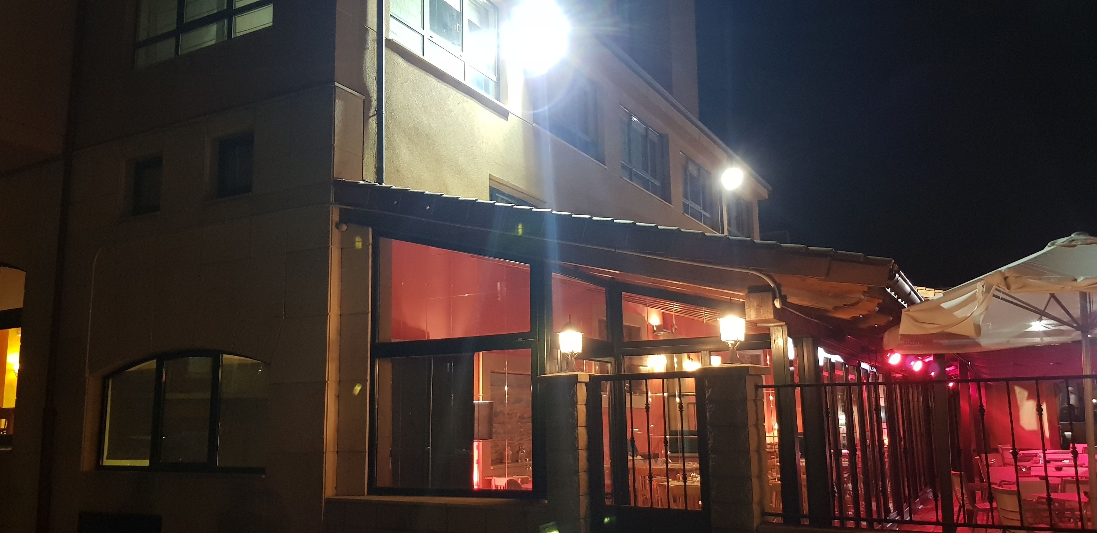 A building with a glass entrance, a red-lit interior, and outdoor seating with umbrellas.