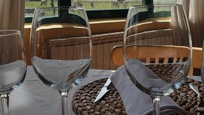 Une table avec deux verres à vin et une serviette, placée devant une fenêtre donnant sur un paysage rural.