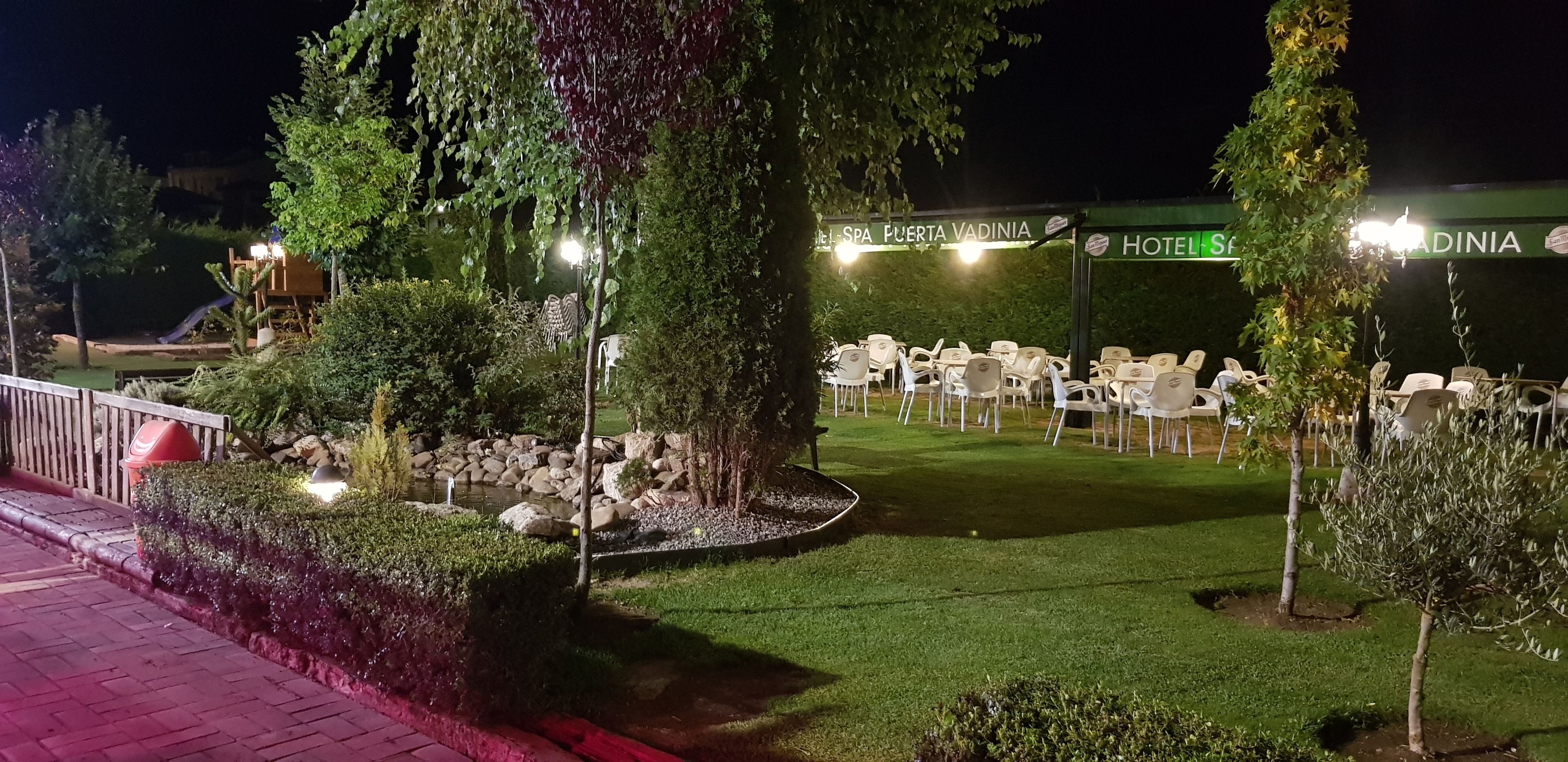 Ein Sitzbereich im Freien mit weißen Plastikstühlen, angeordnet um einen kleinen Garten mit Steinen und Bäumen.