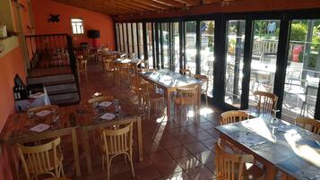 Een restaurant met houten tafels en stoelen, grote ramen en een betegelde vloer.