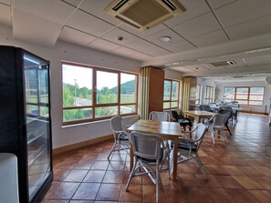 A spacious room with large windows, a tiled floor, and several tables and chairs.
