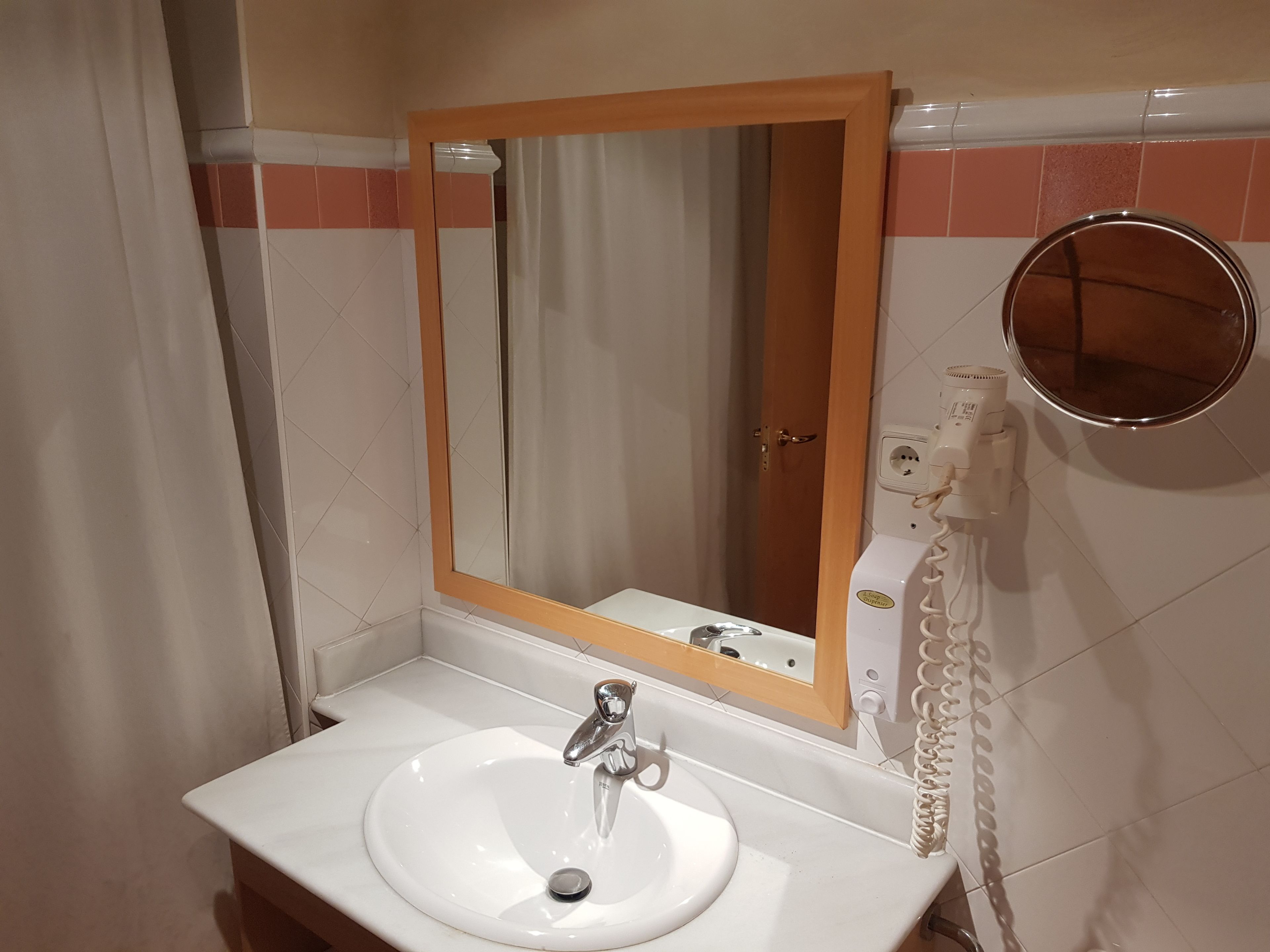 Un baño con un lavamanos blanco, un espejo y un teléfono.