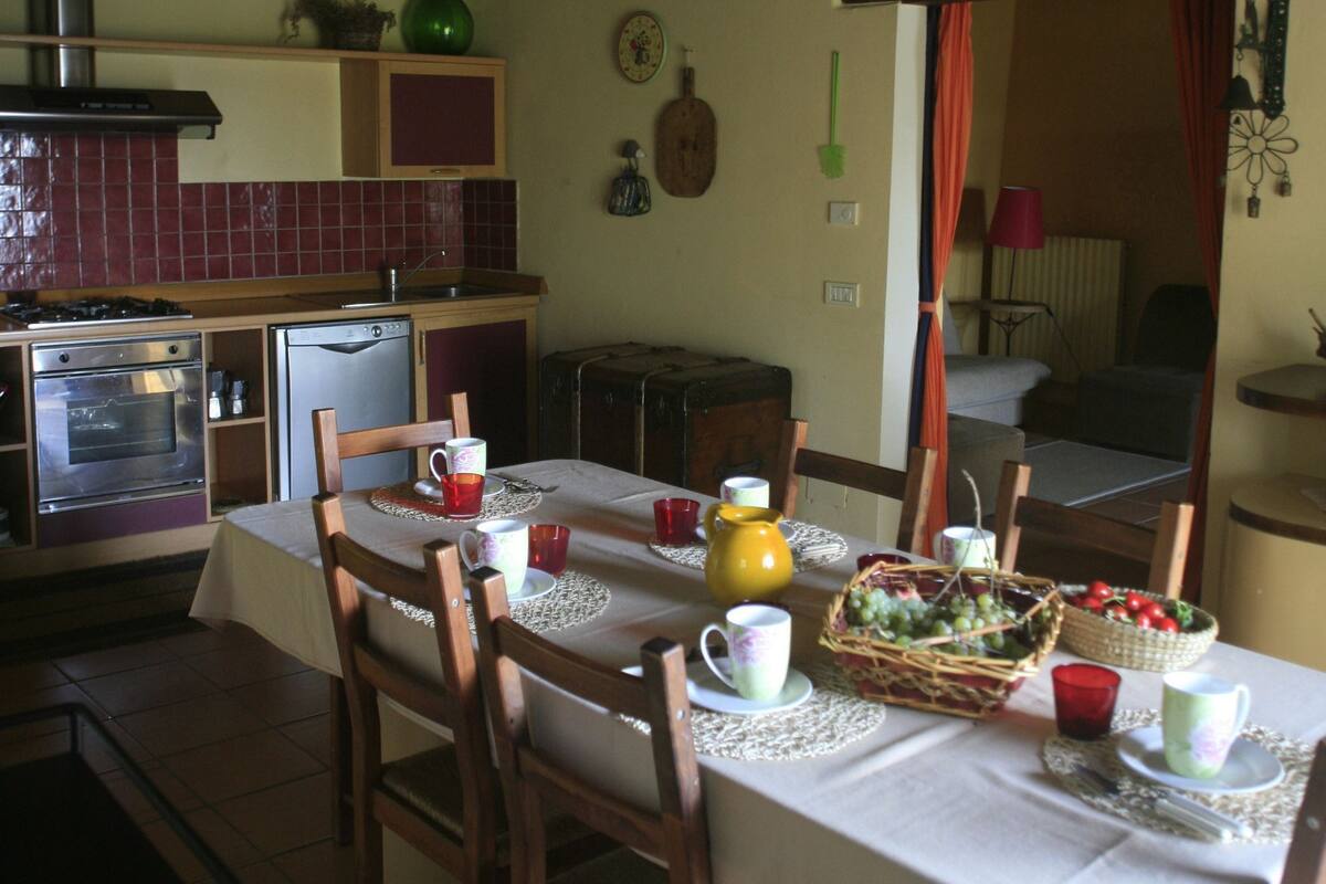 A rustic kitchen with wooden beams, a dining table set with chairs, and a variety of kitchen appliances.