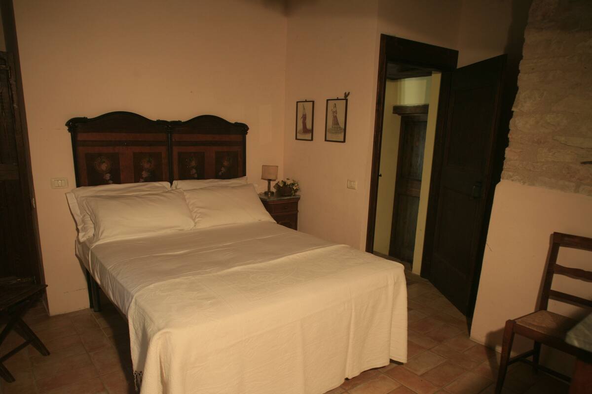 A bedroom with a wooden bed, a nightstand with a lamp, and two framed pictures on the wall.