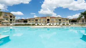 Piscina com espreguiçadeiras e um edifício com várias varandas ao fundo.