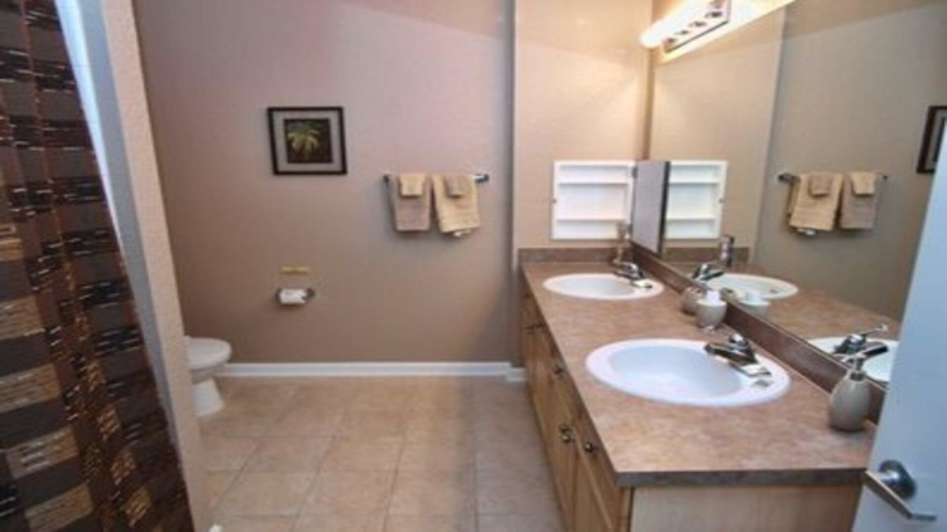 Un baño con dos lavamanos, un inodoro y un espejo.