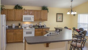 A kitchen with wooden cabinets, a microwave, stove, and a granite countertop island with a sink. - Ip60305 - Highgate at Legacy Park - 4 Bed 3 Baths Villa (Davenport)