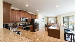 A kitchen with granite countertops, wooden cabinets, stainless steel appliances, and a large island with a sink. - Je63118 - The Encore Club Resort - 6 Bed 5.5 Baths Villa (Kissimmee)