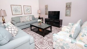 A living room with a sofa set, a coffee table, a TV, and decorative wall art. - Fv62387 - The Dales at West Haven - 7 Bed 6 Baths Villa (Davenport)