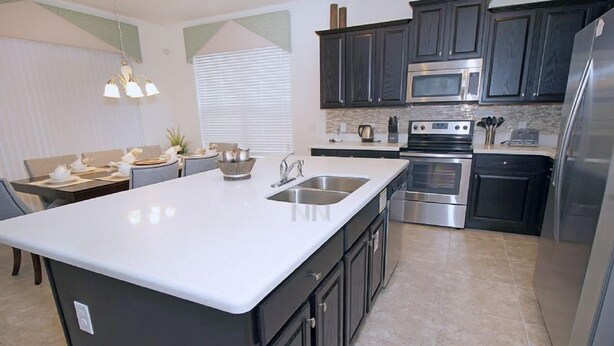 A modern kitchen with dark cabinets, stainless steel appliances, and a white countertop. - Fv62387 - The Dales at West Haven - 7 Bed 6 Baths Villa (Davenport)