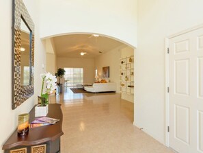 Un passadís ampli amb una porta blanca a la dreta, un sofà blanc al fons i un mirall decoratiu a l'esquerra.