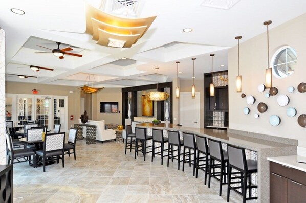 A spacious dining area with a long counter and multiple chairs, a ceiling fan, and pendant lighting.