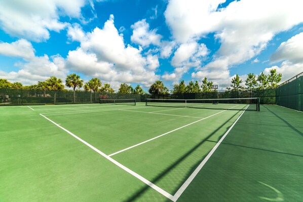 Una cancha de tenis con una red, rodeada de árboles y un cielo despejado.