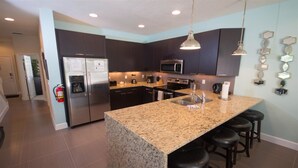 Una cocina moderna con armarios oscuros, encimeras de granito, electrodomésticos de acero inoxidable y una isla central con taburetes de bar.